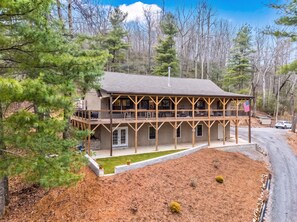 A two-story wooden cabin with a balcony, surrounded by trees and a clear sky. - Peaceful Mountain Retreat | Wraparound Deck (Black Mountain)