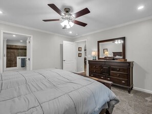 A bedroom with a bed, a dresser, a ceiling fan, and a door leading to a bathroom. - Peaceful Mountain Retreat | Wraparound Deck (Black Mountain)