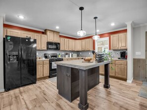 Una cucina moderna con mobili in legno, un frigorifero nero, un forno a microonde, un fornello e luci a sospensione.