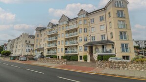 A multi-story residential building with balconies, a stone wall, and a clear road in front. - Beach View Apartment (Colwyn Bay)