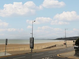Una carretera costera con una playa al fondo, una acera para peatones y un semáforo.