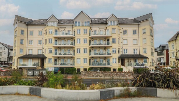 A multi-story residential building with balconies, a paved area in front, and a stone wall. - Beach View Apartment (Colwyn Bay)