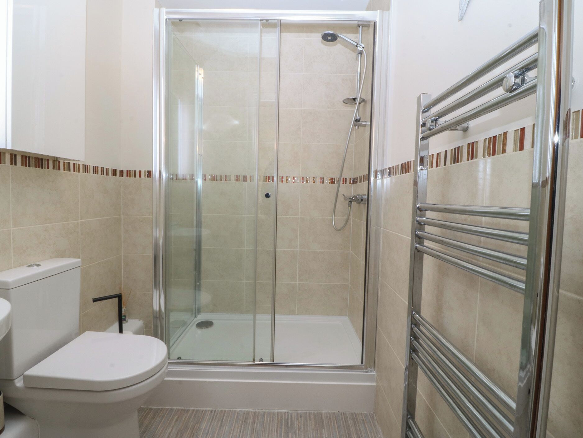 A bathroom with a glass-enclosed shower, a toilet, and a towel rack.