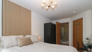 A bedroom with a large bed, a wooden slat wall, a black wardrobe, a glass shower, and a desk with a chair. - Beach View Apartment (Colwyn Bay)