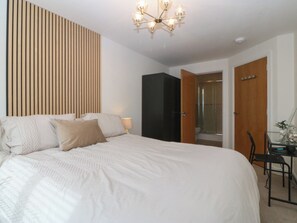 Ein Schlafzimmer mit einem großen Bett, einer Wand aus Holzslattern, einem schwarzen Kleiderschrank, einer Glasdusche und einem Schreibtisch mit Stuhl.