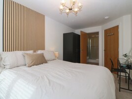 Un dormitorio con una cama grande, un cabecero de listones de madera, un armario negro, cabina de ducha de vidrio y un escritorio con silla.