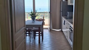 A doorway leading to a dining area with a table and chairs, a kitchen area with cabinets and appliances, and a view through a glass door to the outside.