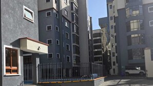 Un edificio residenziale a più piani con un cortile lastricato, cancelli in metallo e cielo sereno.