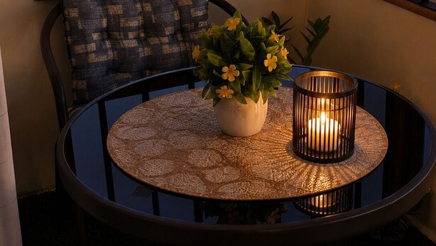 Un tavolo rotondo con tovaglia decorata, una pianta in vaso con fiori gialli e una candela in un portacandele di metallo.