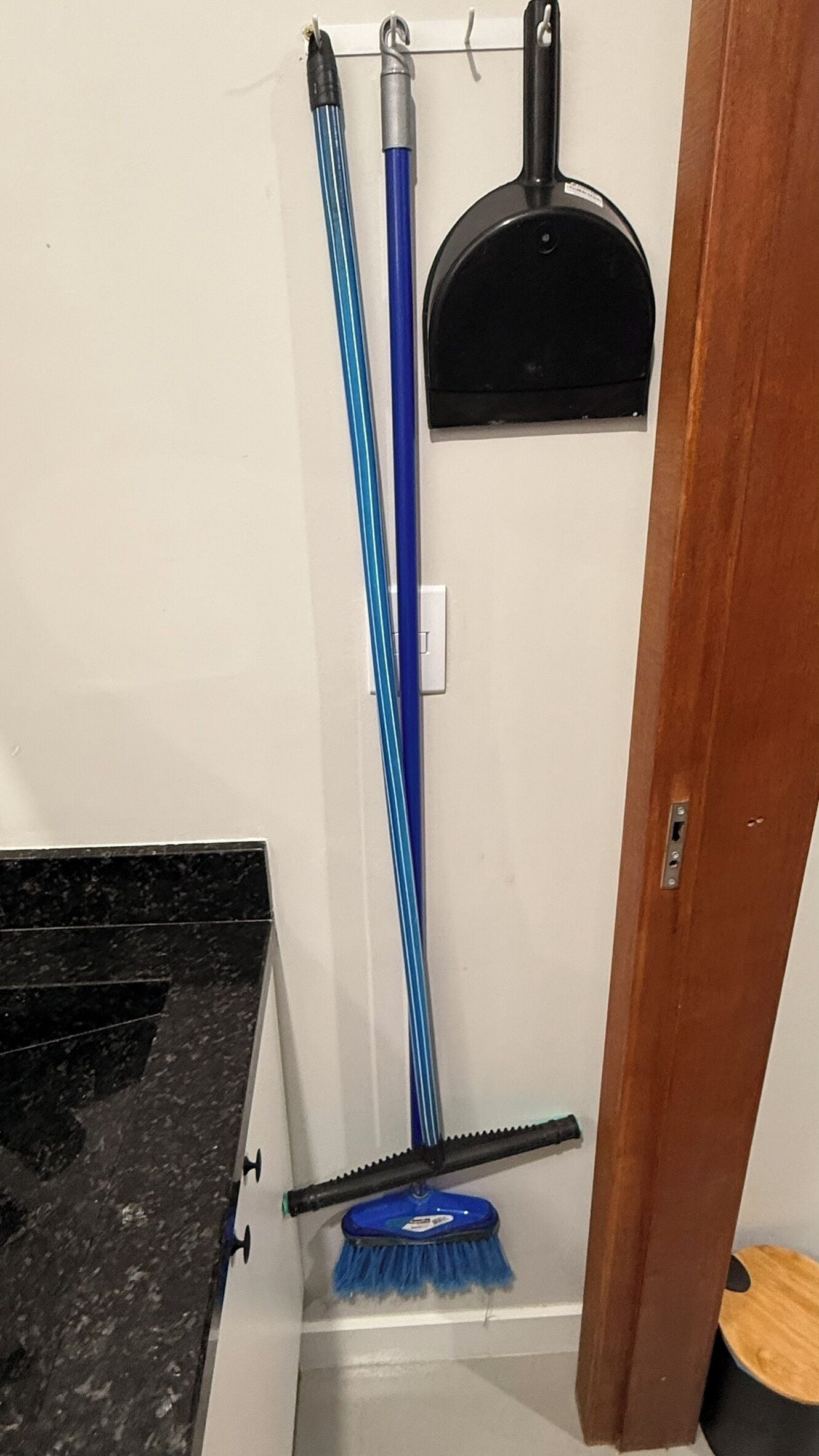 A corner of a room with a black countertop, a blue broom, a black dustpan, and a white wall.