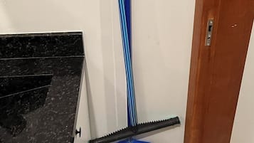 A corner of a room with a black countertop, a blue broom, a black dustpan, and a white wall.