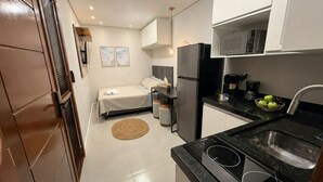 Habitación pequeña con cama, kitchenette y baño reducido.