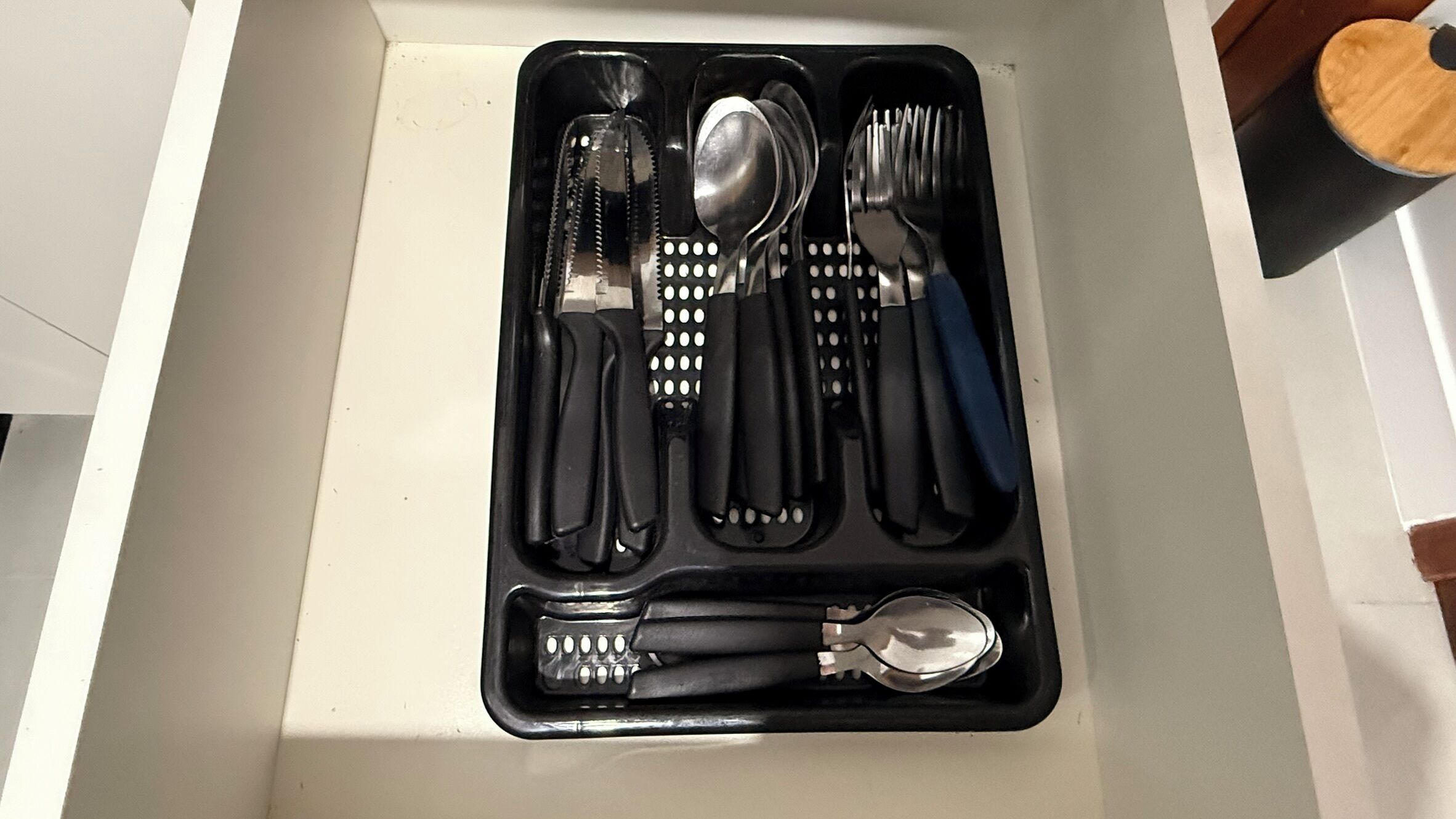 A drawer with a utensil set including knives, spoons, and a grater.