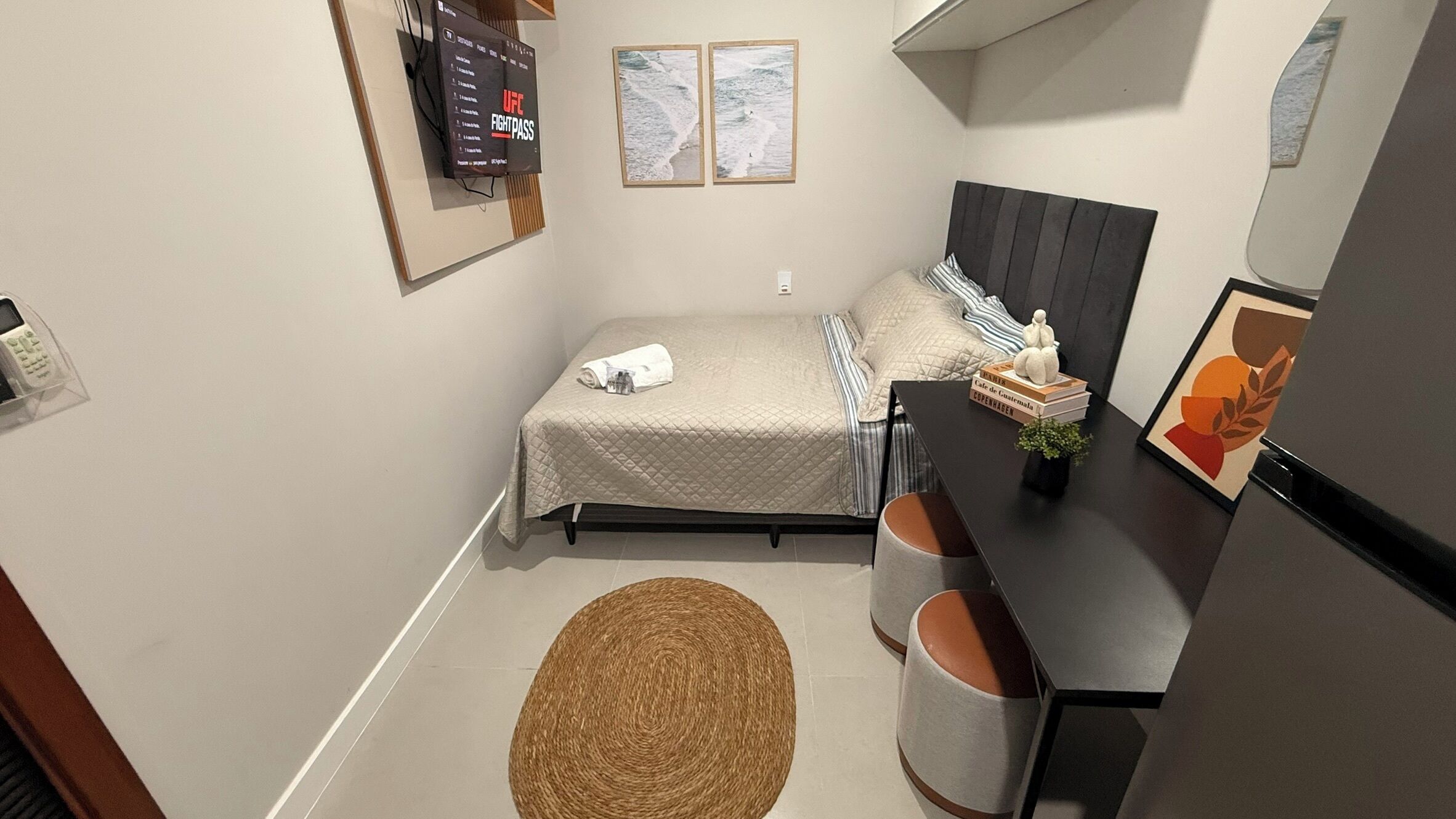 Een compacte, moderne slaapkamer met een bed, nachtkastje en een aan de muur bevestigde televisie.