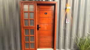 Una puerta de madera con un panel de vidrio, una placa con número, un cartel de prohibido fumar y una lámpara fijada a la pared.