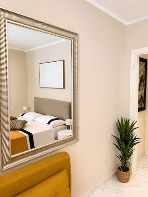 Une chambre d’hôtel avec un grand miroir, un lit avec une literie blanche, une table de chevet avec une lampe et une plante en pot.