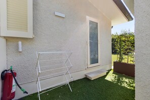 A residential exterior with a white exterior wall, a window, a door, a metal drying rack, and a red fire extinguisher. - Forte Privé • Apartment with Private Garden (Forte dei Marmi)
