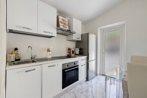 A modern kitchen with white cabinetry, a stainless steel refrigerator, and a built-in oven. - Forte Privé • Apartment with Private Garden (Forte dei Marmi)