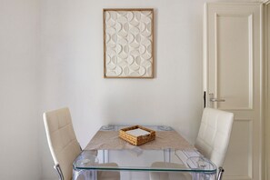 A dining area with a glass table, two chairs, a woven basket, and a decorative wall piece.