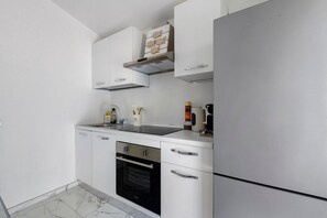 A compact kitchen with white cabinetry, a built-in oven, a stainless steel refrigerator, and a coffee maker on the counter.