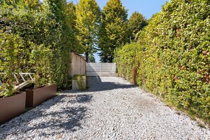 Camí de grava que condueix a una entrada tancada per vegetació densa.