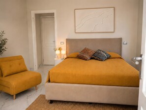 Ein Schlafzimmer mit Bett, Nachttisch, Lampe, Stuhl und einer Tür.