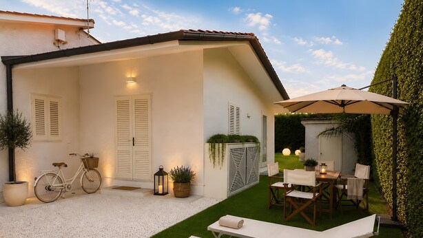 Un patio con una bicicleta, mobiliario exterior y una pared blanca con contraventanas.