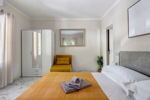 A hotel room with a bed, a sofa, a mirror, a wardrobe, and a small plant.