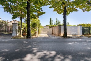 A gated driveway leading to a building with a metal gate and a wooden fence.