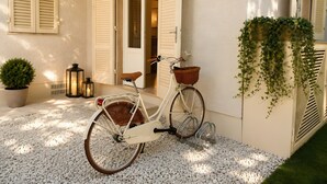 Una bicicleta blanca con una canasta, una planta en maceta y otra colgante cerca de una puerta.