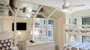 Een slaapkamer met stapelbedden, een dressoir, een televisie en een raam met jaloezieën.