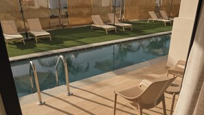 Uma área à beira da piscina com espreguiçadeiras, piscina e uma pequena mesa.