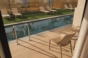 A poolside area with lounge chairs, a pool, and a small table. - Nerion Hotel & Spa (Chania)