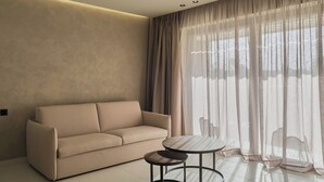Sala de estar moderna com sofá, mesa redonda pequena e cortinas leves.