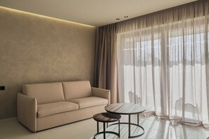 A modern living room with a sofa, a small round table, and sheer curtains. - Nerion Hotel & Spa (Chania)