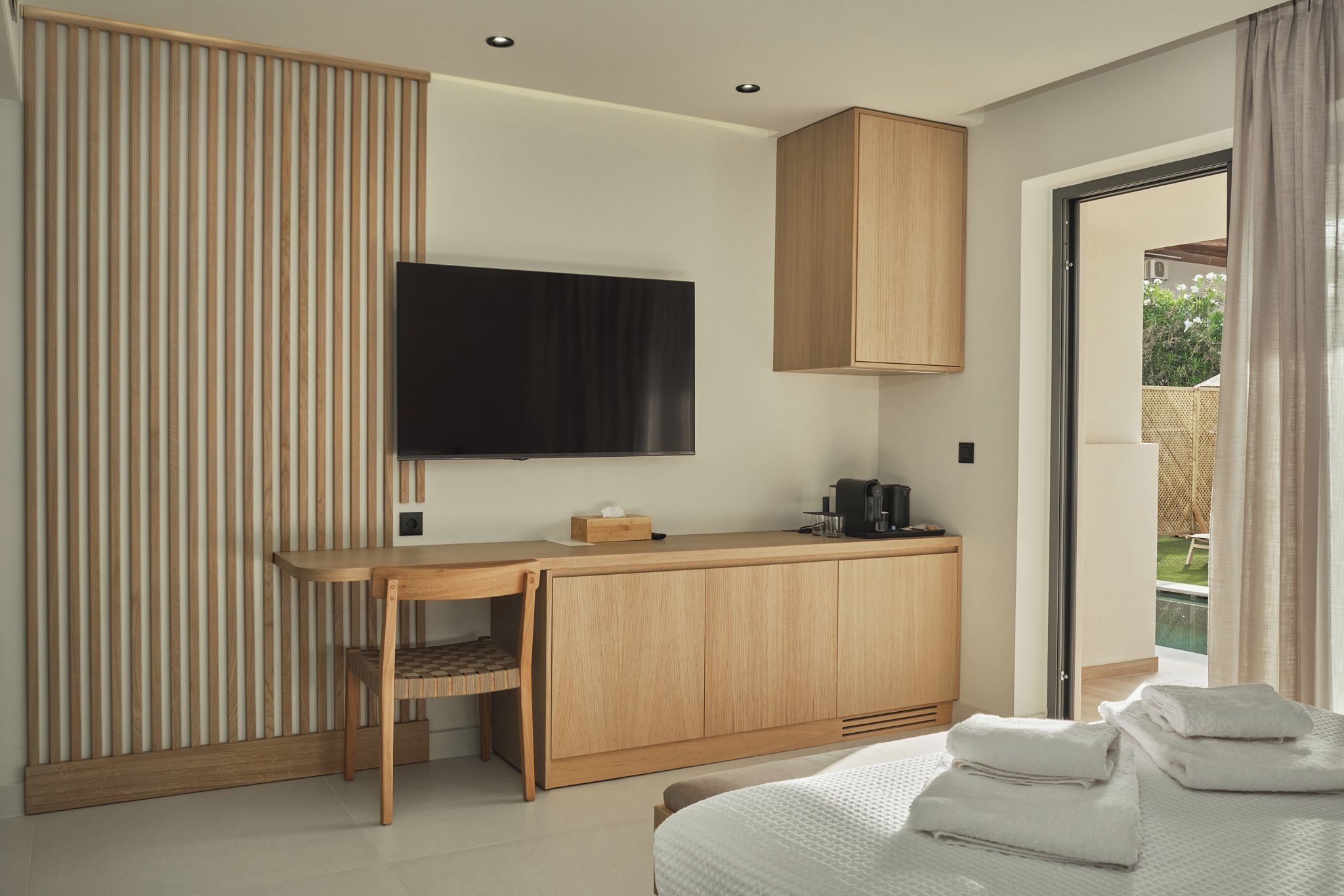 A modern hotel room with a wooden desk, a television, a cabinet, and a bed with towels.