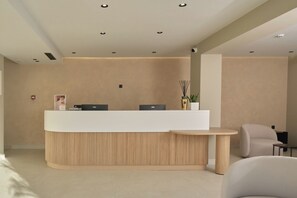 A reception desk with a wooden base and two black monitors, a small round table, and a white chair. - Nerion Hotel & Spa (Chania)