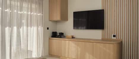 A modern room with a wooden cabinet, a flat-screen TV, a round table, and a window with sheer curtains.