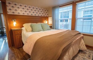 Ein Hotelzimmer mit Bett, Holz-Kopfteil, Nachttischen und einem Fenster mit Jalousien.