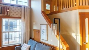 Ein Wohnzimmer mit einer Couch, einer Treppe und einem Fenster mit Vorhängen.
