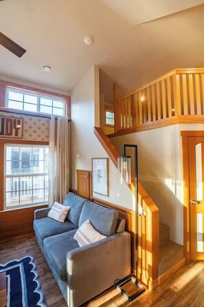 Ein Wohnzimmer mit einer Couch, einer Treppe und einem Fenster mit Vorhängen.