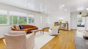 Ein geräumiges Wohnzimmer mit Holzboden, weißen Wänden und großen Fenstern.