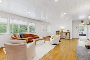 Ein geräumiges Wohnzimmer mit Holzboden, weißen Wänden und großen Fenstern.