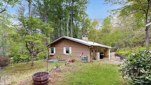 Eine Holzblockhütte mit Veranda, umgeben von Bäumen und einem Rasen.
