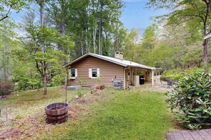 Eine Holzblockhütte mit Veranda, umgeben von Bäumen und einem Rasen.