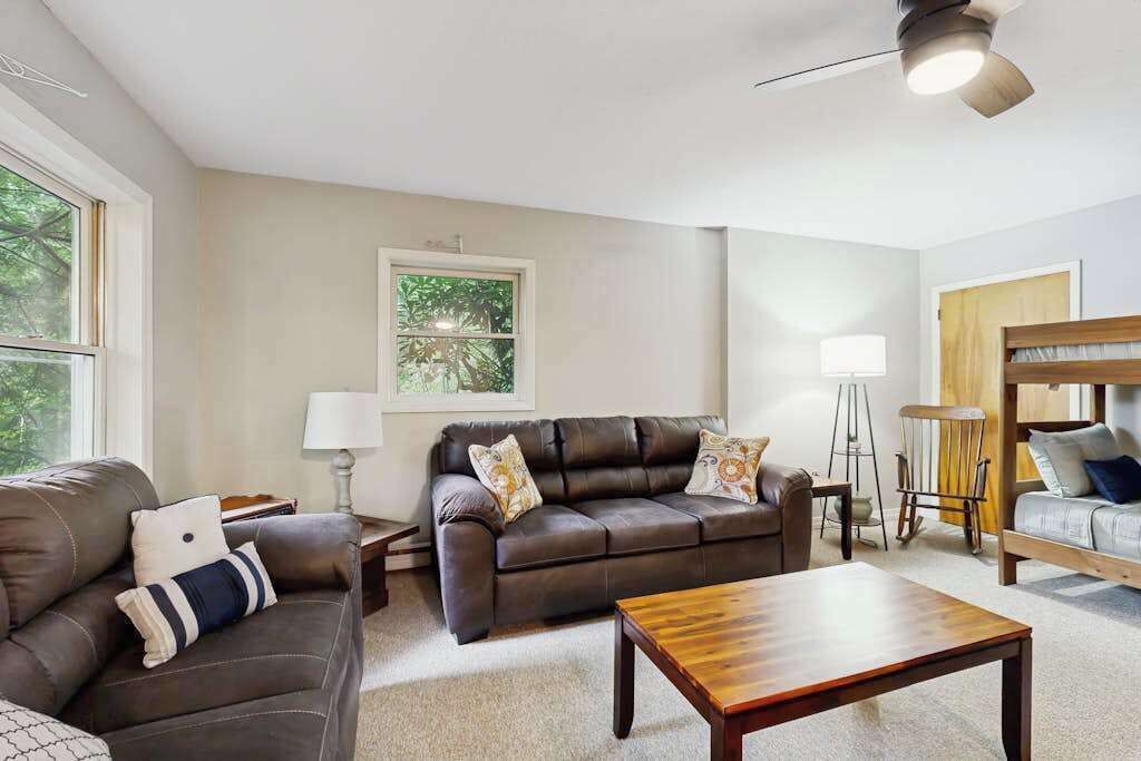 A living room with a brown leather sofa, a wooden coffee table, and a window with a view of trees.