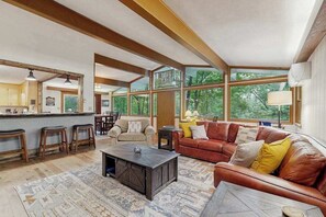 Ein geräumiger Wohnbereich mit großem Fenster, einer Ledersofa, einem Couchtisch und einer Küchenzeile mit Barhocker.