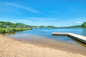 Ein Fluss mit einem Sandstrand und einer hölzernen Anlegestelle, die sich ins Wasser erstreckt.