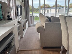 Ein modernes Wohnzimmer mit einer Couch, einem Fernseher und Blick auf einen weißen Zaun und Bäume.