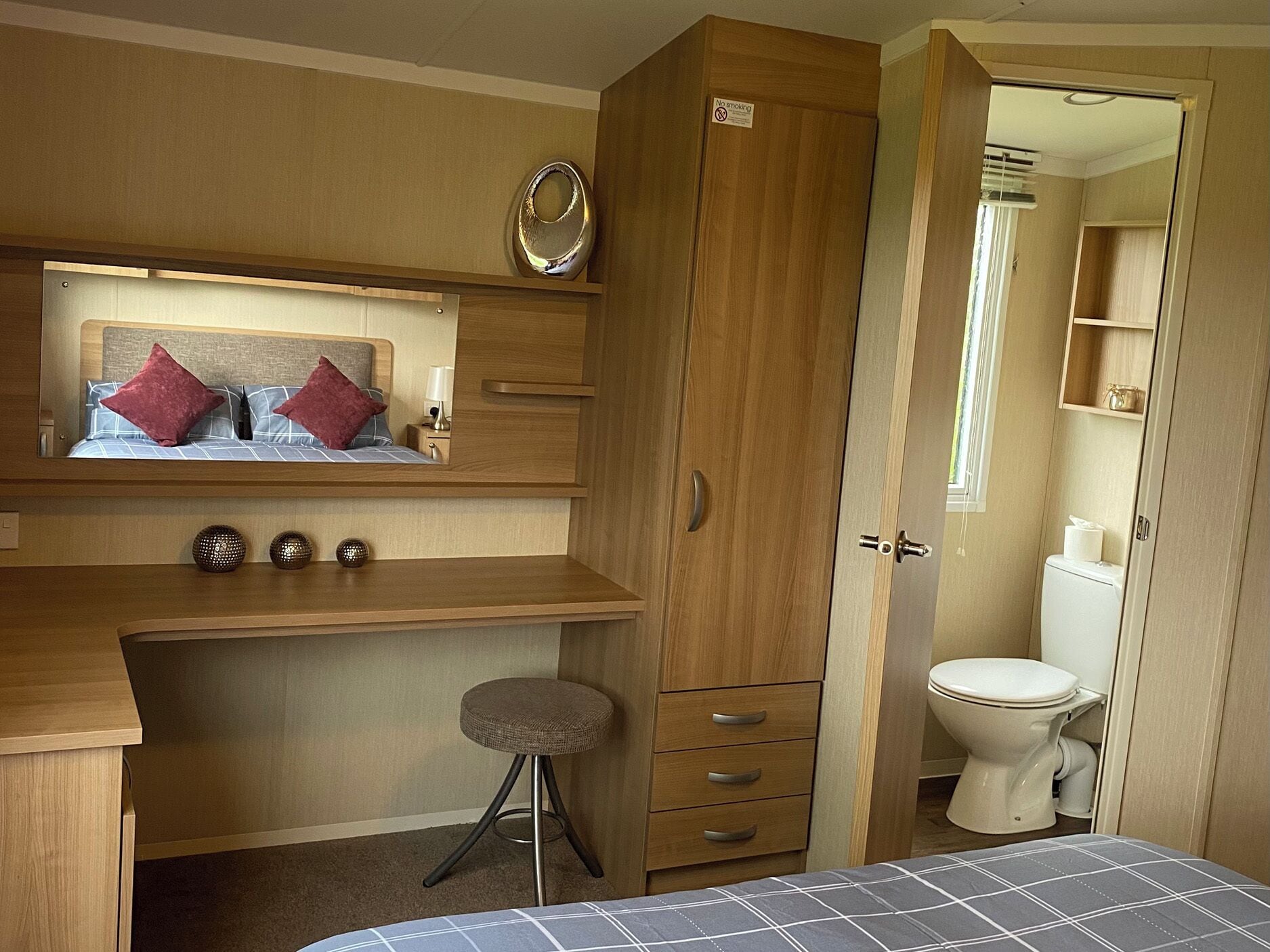 Habitación pequeña con cama, escritorio con espejo, taburete, armario y un inodoro.